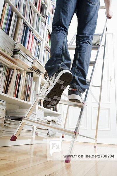 Die Beine eines Mannes klettern auf eine Leiter  die gleich umkippt.
