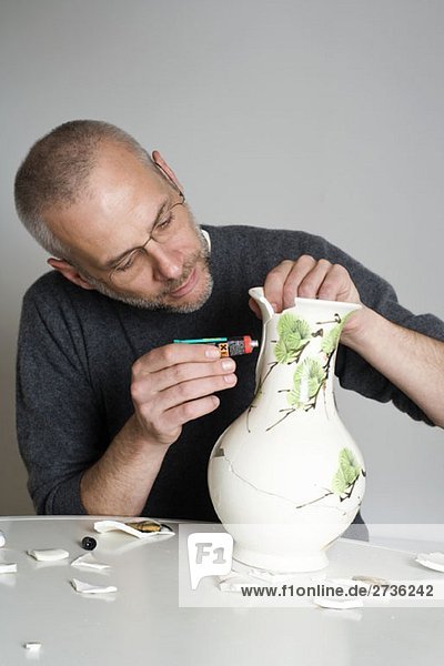 Ein Mann  der eine kaputte Vase repariert.