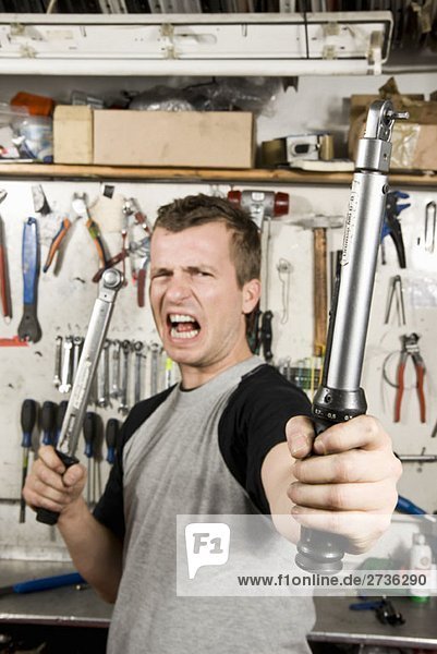 A man holding two socket wrenches and making a face
