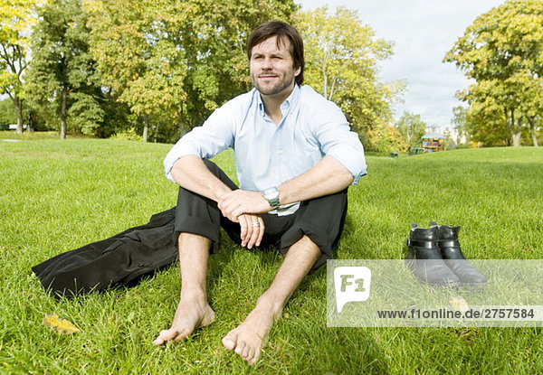 Mann sitzt barfuß auf dem Rasen