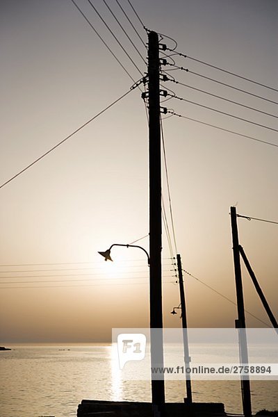 Elektrische Leitungen in den Sonnenuntergang am Meer Griechenland.