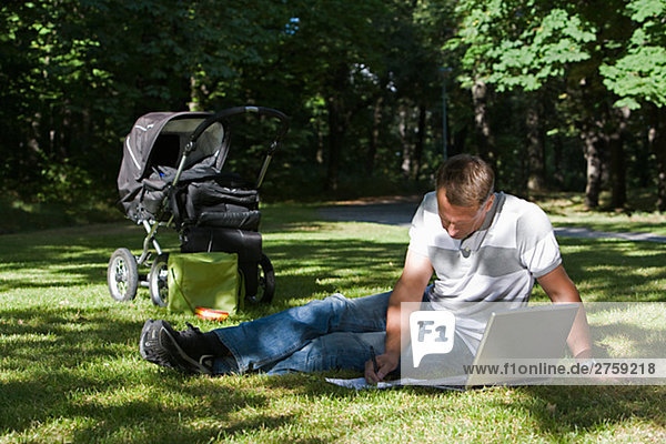 A man with a pram and a computer in a park a sunny day Sweden.