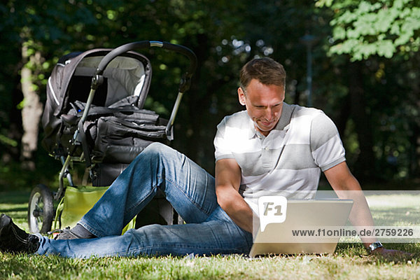 A man with a pram and a computer in a park a sunny day Sweden.
