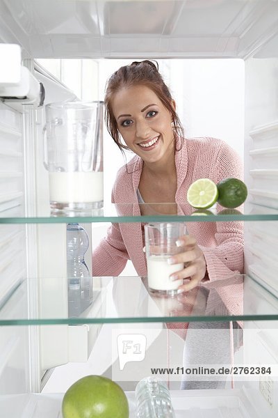 Portrait of young woman putting milkglass in refrigerator and smiling