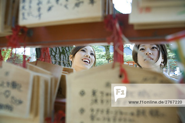 Junge Frauen beim Betrachten traditioneller japanischer Ema-Wünsche im Shinto-Schrein