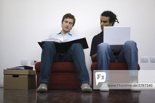 Men working side by side  one with laptop  one with binder