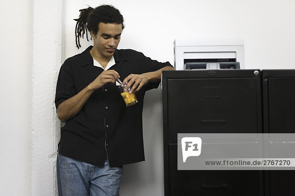 Man leaning against filing cabinet  stirring drink