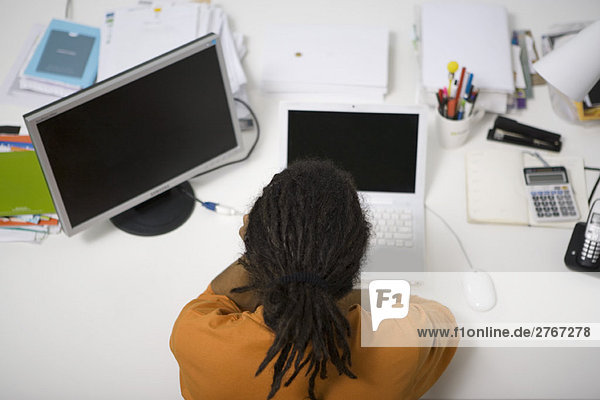 Man with dreadlocks working at desk  rear overhead view