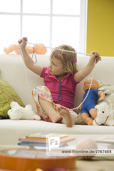Kleines Mädchen sitzend auf Sofa mit Spielzeug  spielend mit Modeschmuck