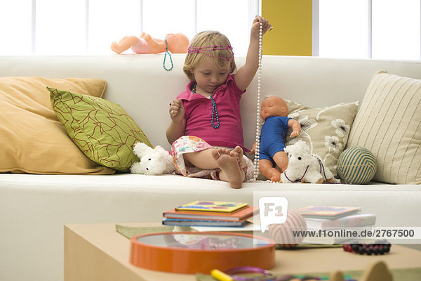 Kleines Mädchen spielt mit Spielzeug und Modeschmuck auf dem Sofa