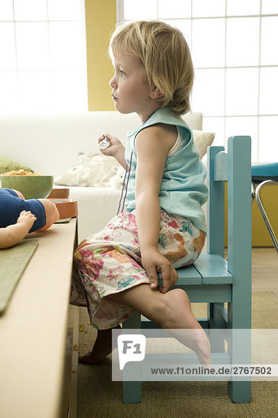 Kleinkind Mädchen am Tisch sitzend  Knöchel berührend  Seitenansicht
