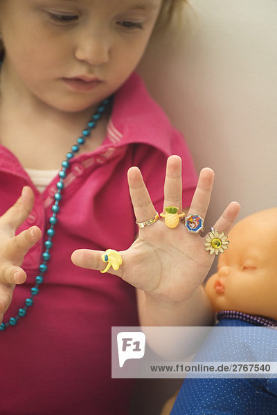 Kleines Mädchen mit Plastikringen an jedem Finger  schaut auf die Hand.