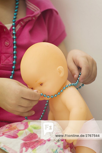Kleines Mädchen setzt Halskette auf Babypuppe  abgeschnittene Ansicht