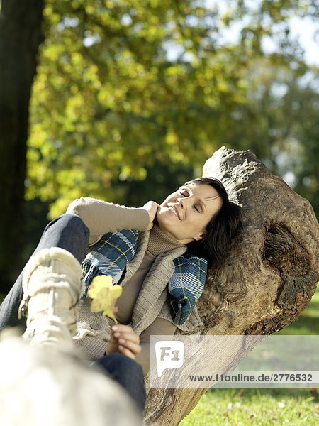 Reife Frau ruht auf abgefallener Baum und lächelnd
