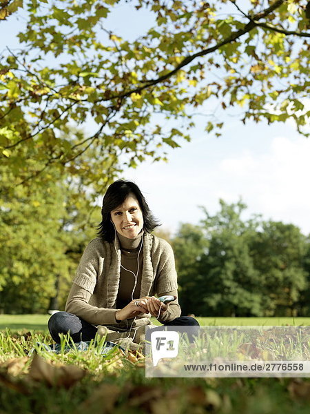 Portrait reife Frau anhören von mp3-Player im park