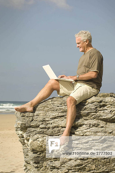 Ein Mann am Strand  der seinen Computer benutzt.