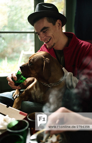 Young man letting pet dog drink from glass