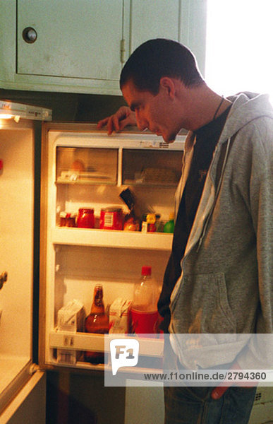 Junger Mann steht vor offenem Kühlschrank