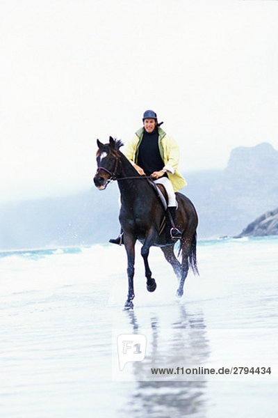 Mann reitet Pferd am Strand