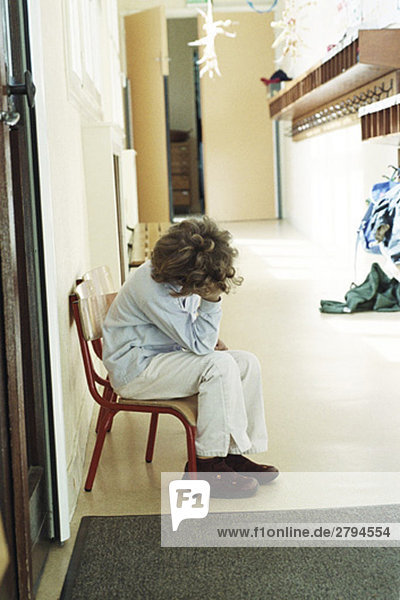 Child sitting alone in corridor  holding head