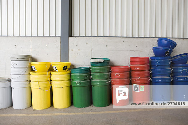 Mehrfarbige Mülltonnen und Recyclingbehälter an der Wand gestapelt