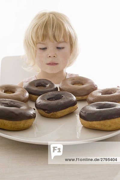 Kleines Mädchen sitzt vor einem Teller mit Doughnuts