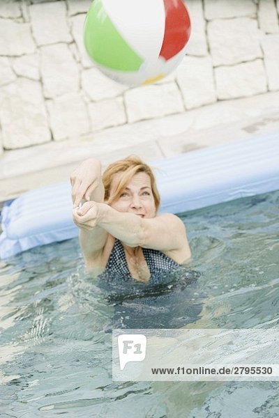 Blonde Frau spielt mit einem Wasserball im Schwimmbecken