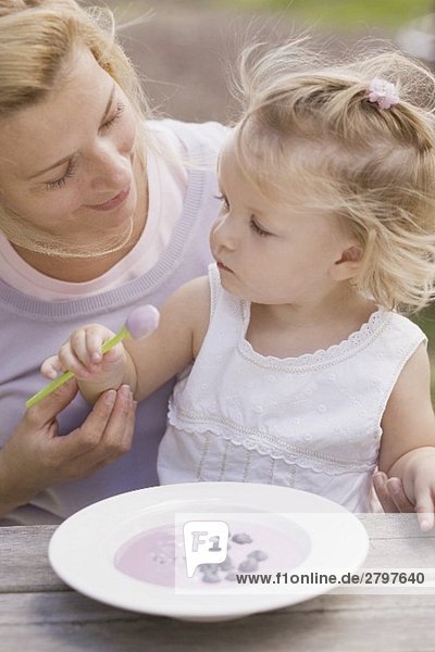 Mutter und kleine Tochter mit einem Teller Heidelbeerjoghurt