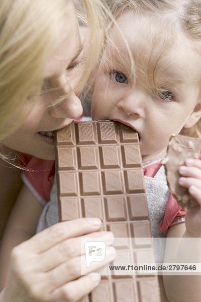 Mutter und kleine Tochter beissen in eine Tafel Schokolade