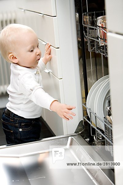 A baby standing by a dishwasher Sweden.