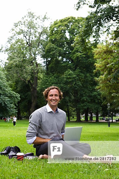 Ein Mann mit einem Laptop in einem Park Schweden.