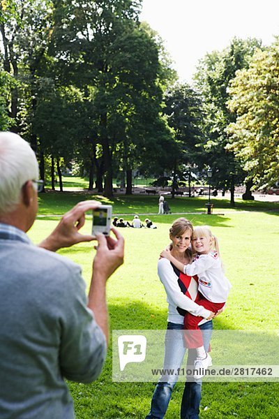 Woman senior man and girl taking photographs in the park Sweden.