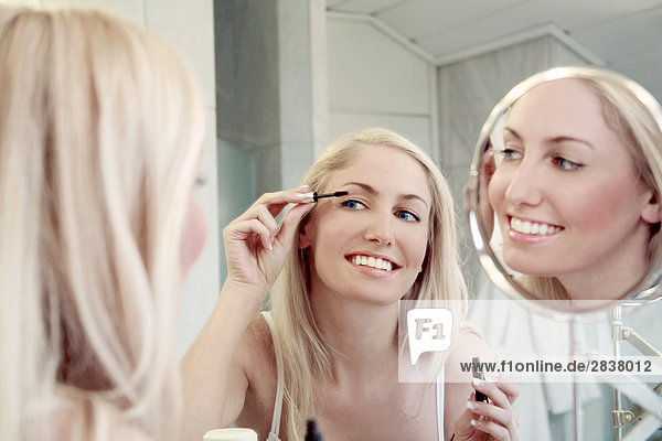 Reflexion der junge Frau Anwendung Mascara in Spiegel