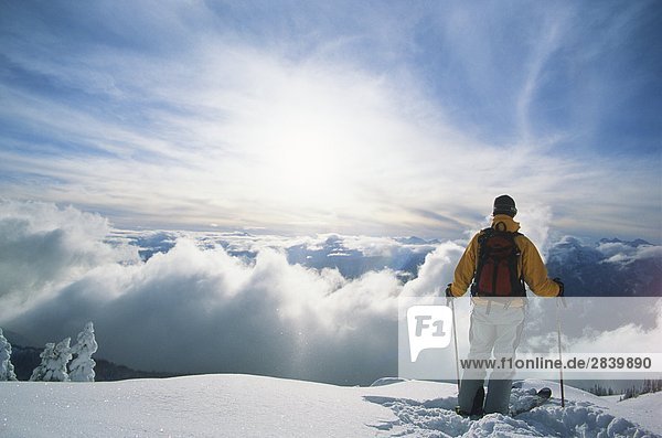 a backcountry skier admiring the view above the clouds and high on a mountain in the Selkirk Range  British Columbia  Canada.