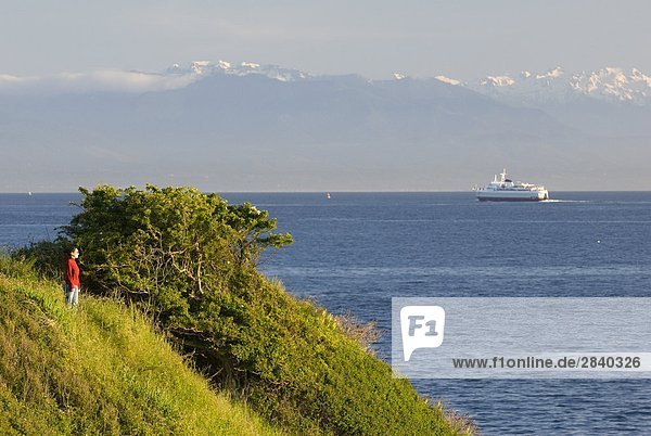 A woman enjoying the view along the Dallas Road waterfront as the Coho Ferry passes in the distance in Victoria  Vancouver Island  British Columbia  Canada.