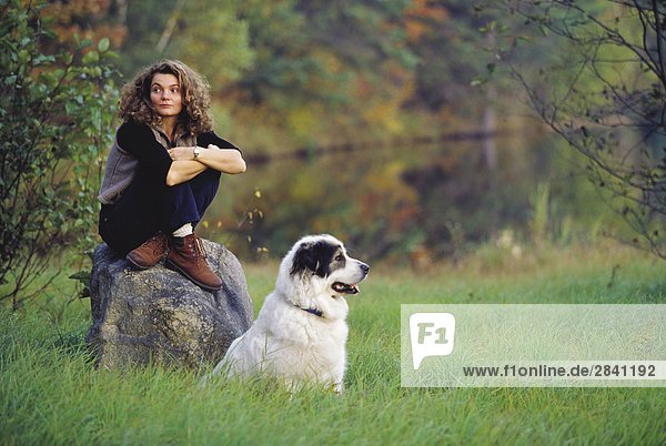 27 Jahre alte hellhäutige Frau sitzend auf einem Felsen mit einem großen Pyranee Hund während der Herbst-Saison  Saint Calixte  Québec  Kanada.