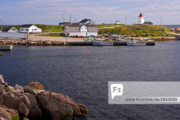 Boats docked in Neils Harbour with the Neils Harbour Lighthouse on Neils Harbour Point  Cabot Trail  Cape Breton  Nova Scotia  Canada.