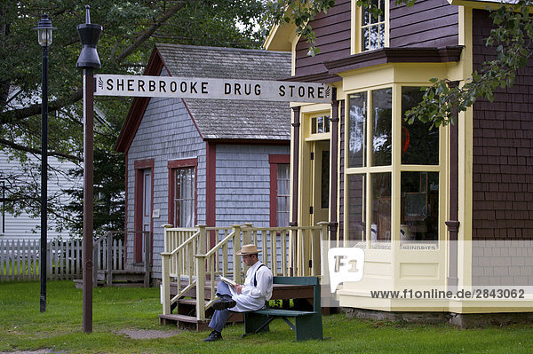 Ein kostümierten Mann sitzt außerhalb der Sherbrooke Drogerie entlang der Hauptstraße  Wharf Road  in Sherbrooke Dorfmuseum (eine restaurierte 1860 Stampfender Schiffbau Gemeinschaft und) in der Stadt von Sherbrooke entlang dem Marine-Antrieb  Highway 7  Nova Scotia  Kanada.