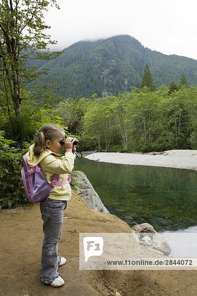 Little girl looking through binoculars on a hiking trail at Golden Ears Provincial Park in Maple Ridge  British Columbia  Canada