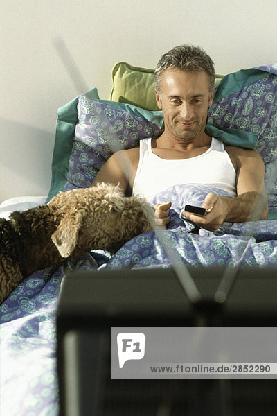 Mann beim Fernsehen im Bett mit Hund