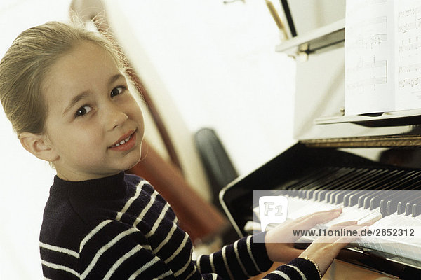 Mädchen spielt Klavier  schaut in die Kamera.