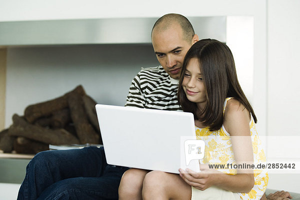 Vater und Tochter schauen zusammen auf den Laptop.