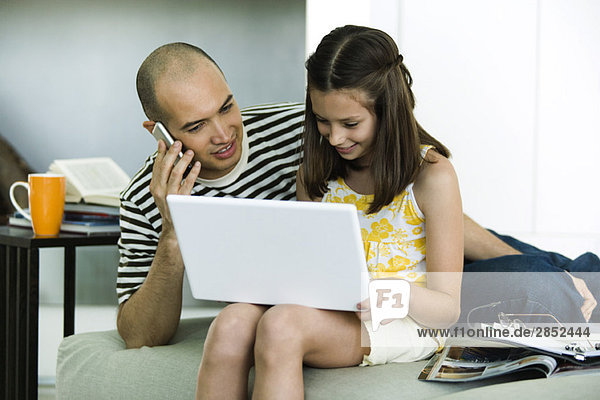 Father and daughter looking at laptop computer together  man using cell phone