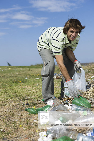 Young male picking up trash in field