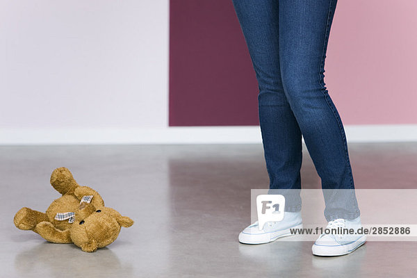 Junge Frau steht neben Teddybär auf dem Boden  niedrige Sektion