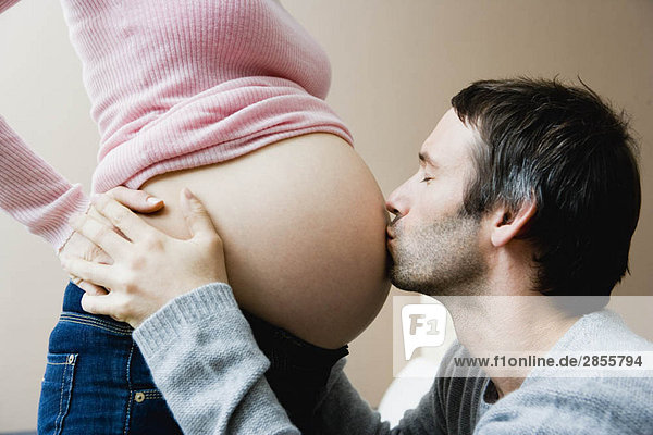 Mann  der den schwangeren Magen einer Frau küsst.