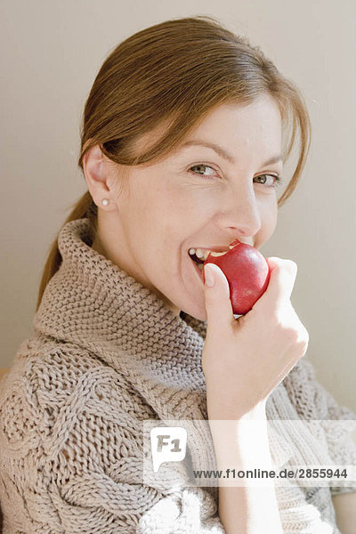 Frau lächelt den Zuschauer an und isst einen Apfel.