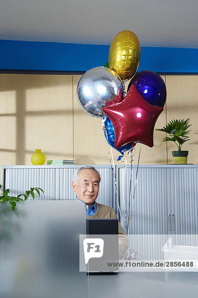 Senior mit Luftballons am Schreibtisch