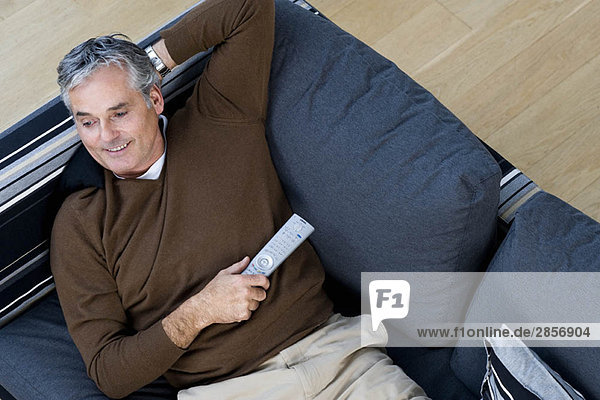Mann entspannt auf Sofa mit TV-Fernbedienung