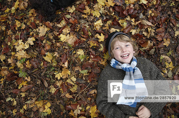 Junge auf Herbstblättern liegend